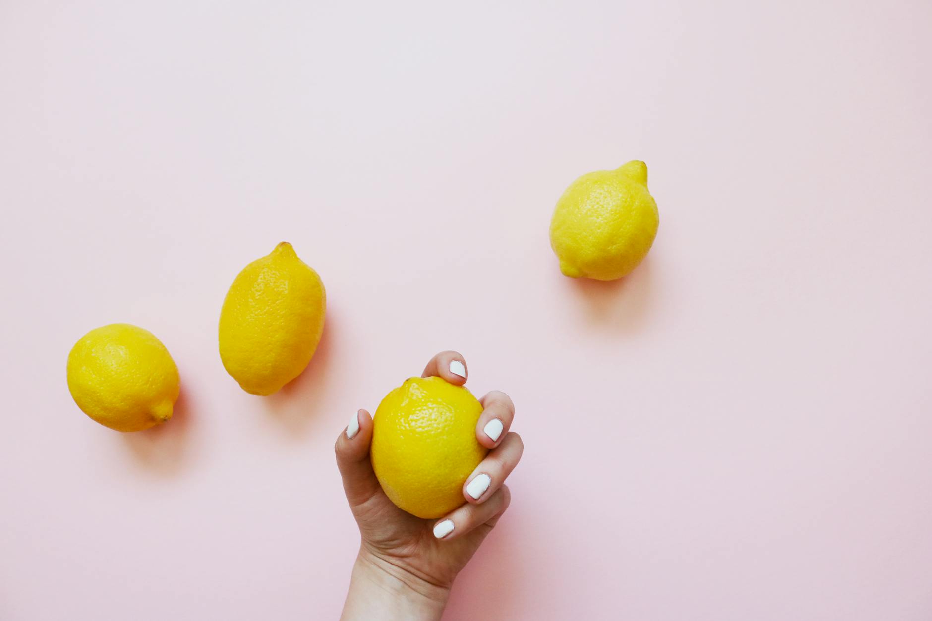 Une main tenant un citron sur fond rose doux, entourée de trois citrons supplémentaires.