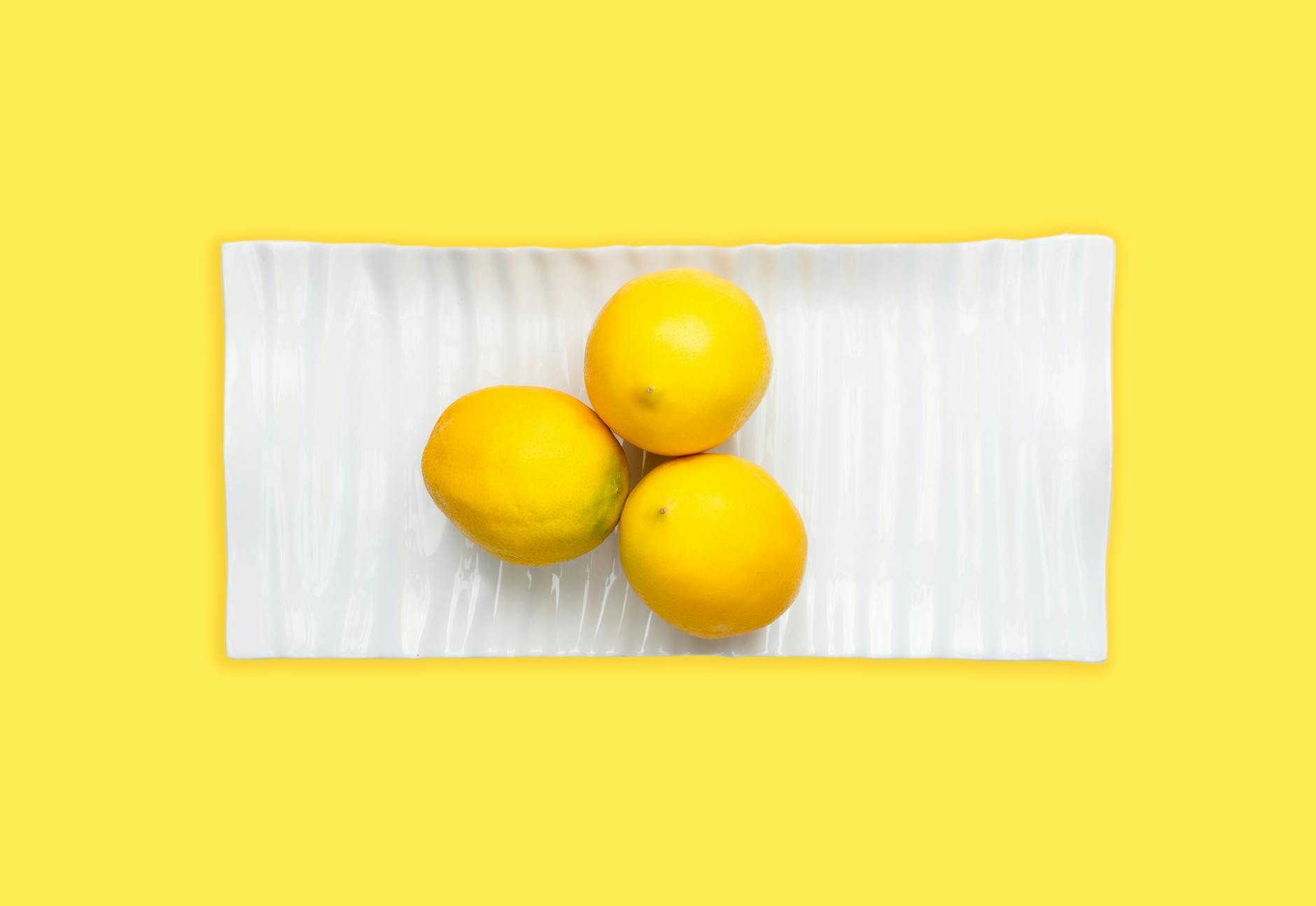 Frische Zitronen auf weißem Teller mit leuchtend gelbem Hintergrund, die Frische und klitorale Stimulation symbolisieren