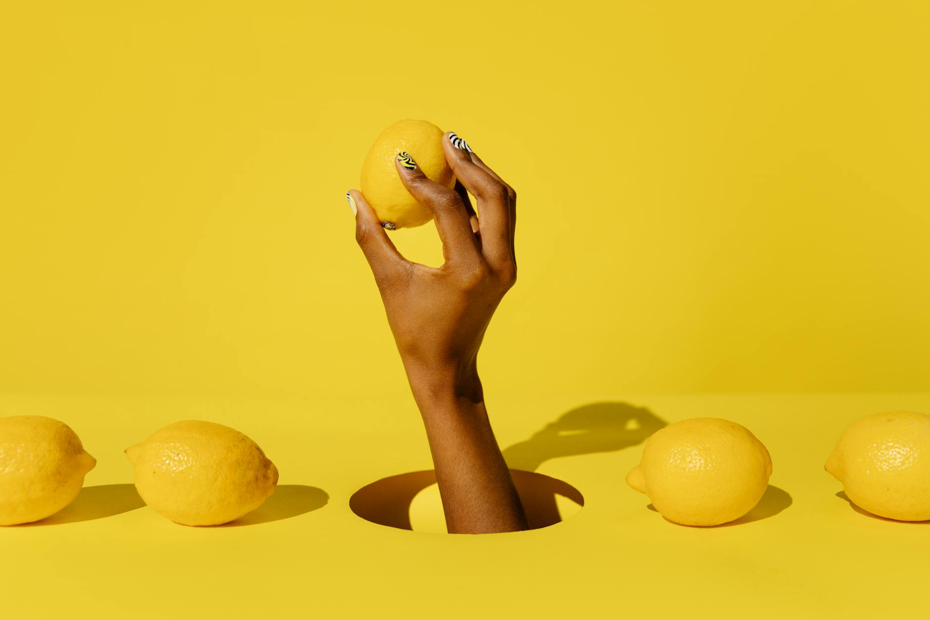 Une main tenant un citron vibrant sur un fond jaune ensoleillé, symbolisant l'énergie et la fraîcheur
