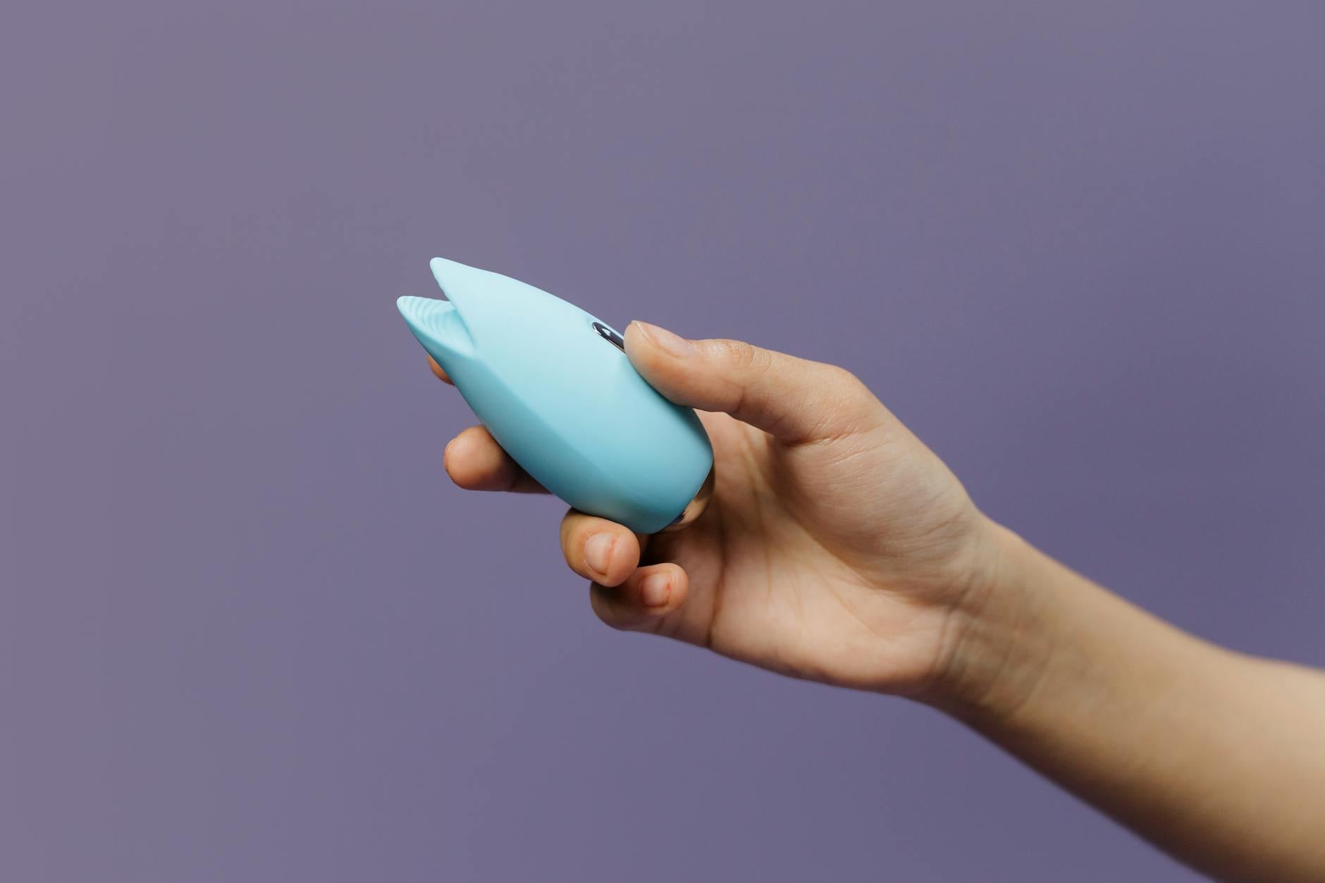 Handgehaltener blauer Silikon-Vibrator vor lila Hintergrund, zeigt Selbstliebe und Sexualität