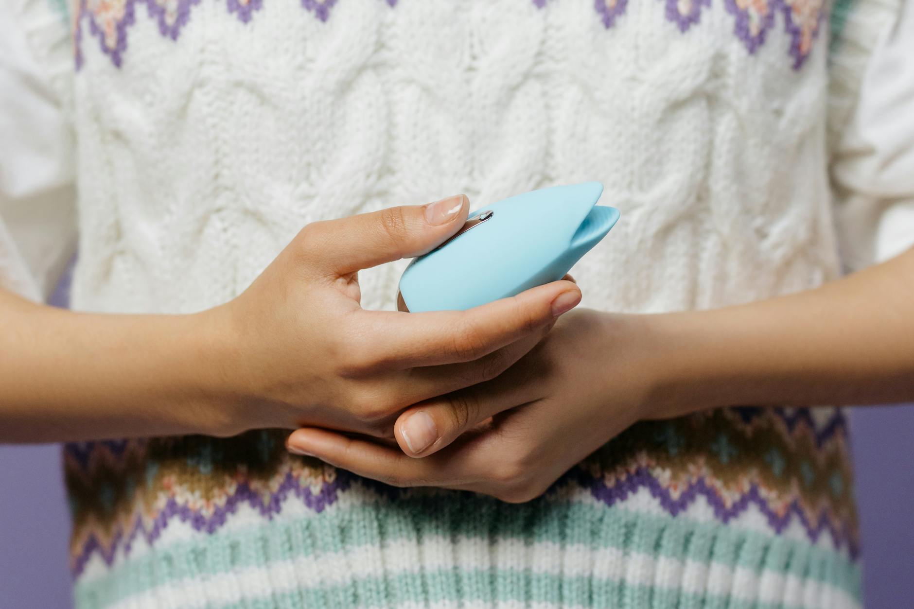 Gros plan des mains tenant un vibrateur bleu personnel contre un pull en tricot.