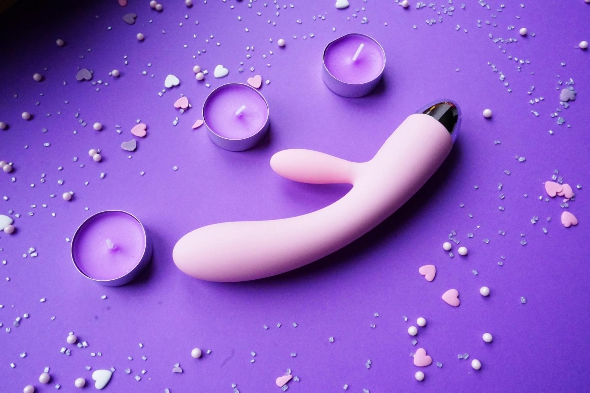 Vibrateur rose sur un fond pourpre avec confettis en cœurs et bougies pour une ambiance romantique