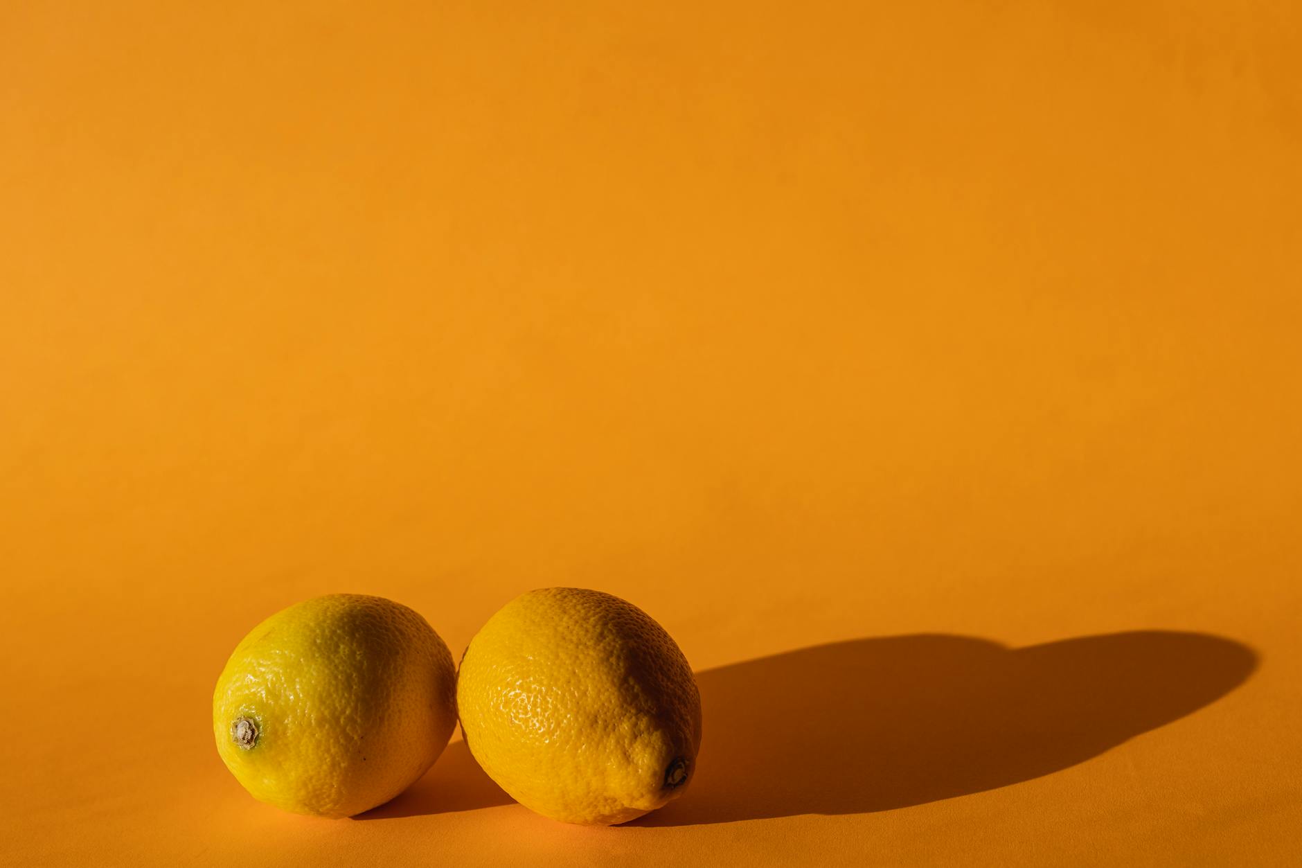 Une main tenant un citron frais sur un fond rose pastel, entourée de trois autres citrons brillants